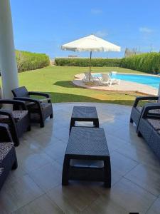 a patio with tables and an umbrella and a pool at فيلا غرناطه الساحل الشمالي in Dawwār al Ḩajj Aḩmad