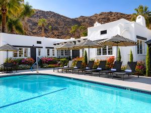 a pool with chairs and umbrellas next to a house at Gloria Palm Springs in Palm Springs