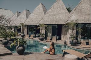 a woman sitting by a swimming pool reading a book at MIZU Boutique Villas - Unique stay in Uluwatu in Uluwatu