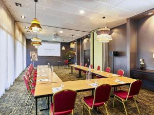 a conference room with long tables and chairs and a screen at Mercure Beaune Centre in Beaune +202 photos