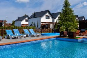 a swimming pool with lounge chairs and a house at Corden Village in Łeba