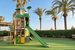 a green slide in a playground with palm trees at Iberostar Waves Málaga Playa in Torrox Costa
