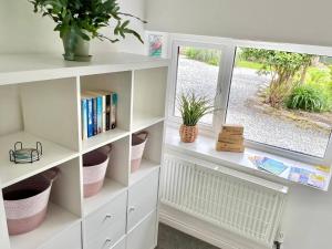 a white book shelf with a window and plants at Hydrangea Cottage in St Austell +14 photos