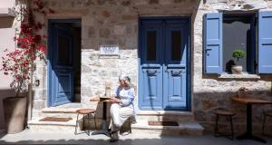 a woman sitting outside of a building with blue doors at BOĒM Boutique Hotel Lefkada in Lefkada +58 photos