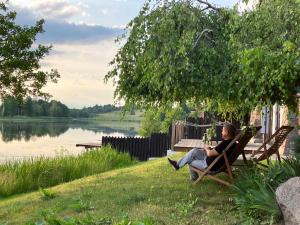 a woman sitting on a bench next to a lake at Dom Nowe Krzywe in Nowe Krzywe