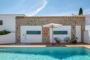 a pool with two chairs and an umbrella next to a house at Chalet Fuente2 piscina común famila in Conil de la Frontera