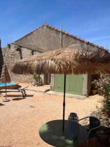 a table with a straw umbrella in a yard at Le Son des Violons in Sallèles-dʼAude