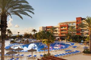 a resort pool with chairs and umbrellas and palm trees at Elba Carlota Beach & Golf Resort in Caleta De Fuste