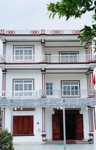a white building with red doors and a tree at Nhà nghỉ Thảo Thảo Quan Lạn Minh Châu in Quang Ninh