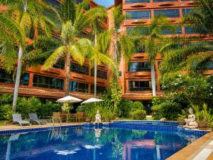 a swimming pool in front of a building with palm trees at Nova Park Hotel Pattaya in Pattaya