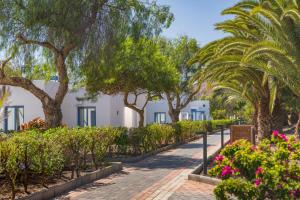 a walkway with trees and flowers in front of white houses at Elba Premium Suites - Adults Only in Playa Blanca