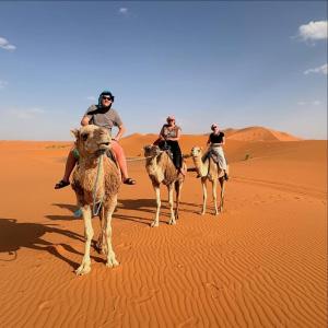 three people riding on camels in the desert at Sahara Nomadic Luxury Camp in Merzouga