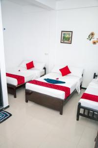 three beds in a room with white walls and red pillows at Alles garden New Seaside in Trincomalee