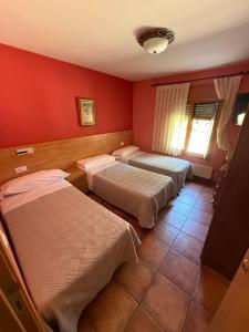 two beds in a room with red walls at Hostal Arévacos in Soria