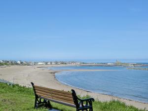 a park bench sitting on the side of a beach at Rothsay Beach House in Newbiggin-by-the-Sea +10 photos