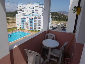 Un balcón con mesa y sillas y una piscina. en Cité Jardins Appartement, en Martil