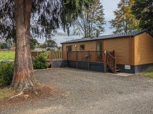 a wooden cabin with a large deck next to a tree at Glenbeagles Lodge in Dollar