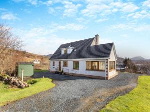 a white house with a black roof on a gravel driveway at Bramble Cottage in Gairloch
