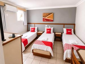 a room with three beds with red pillows at Hotel Teofilo Otoni in Teófilo Otoni