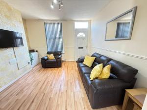 a living room with a black leather couch and yellow pillows at SPACIOUS 3 BEDROOM HOUSE WITH FREE STREET PARKING and WIFI IDEAL FOR CONTRACTORS by NORTH WEST ACCOMMODATION in Saint Helens