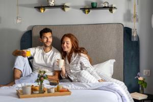 a man and a woman sitting on a bed with drinks at Hôtel Eiffel Saint Charles in Paris