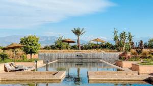 a swimming pool with two chairs and umbrellas at Villa TIGMIZEN - 10CH - Piscine chauffée et Spa - Marrakech in El Aouina