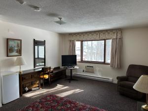 a living room with a television and a desk with a chair at Auberge Eldo Inn in Blind River