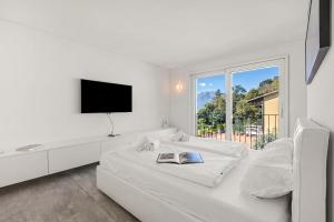 a white bedroom with a white bed and a window at Villa Mondacce with Jacuzzi & Lake Views in Minusio