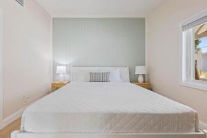a white bed in a white bedroom with two lamps at Anchor House in Cocoa Beach