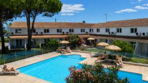 an image of a hotel with a swimming pool and people sitting around it at Artemia Aigues-Mortes - Hôtel avec piscine - Bornes électriques - Parking privé - Local vélo-moto in Aigues-Mortes