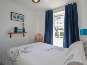 a bedroom with a bed with blue curtains and a window at Tin Lantern Cottage in Redruth