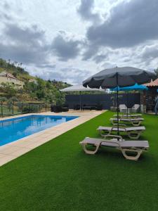 a group of lounge chairs and an umbrella next to a pool at Casa Resineiro com Piscina, Garagem e Terraço in Proença-a-Nova