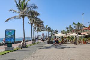 a beach with palm trees and people walking down a sidewalk at Oasis con piscinas y jardines en Maspalomas in Maspalomas