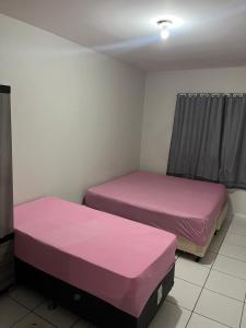 two beds in a room with pink sheets at Quarto família ap5 in Montes Claros