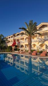 a palm tree in front of a building with a swimming pool at Sunflower Apartments & Studios in Laganas