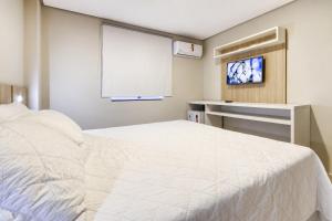 a bedroom with a white bed and a flat screen tv at WR Confort Hotel Campo Grande in Campo Grande