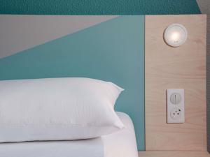 a bed with a white pillow and a lightswitch at ibis Budget Mâcon Sud in Mâcon