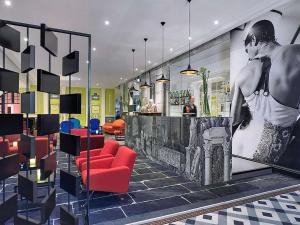 a lobby with a bar with red chairs and a poster at Jules César Hotel & Spa Arles - MGallery Collection in Arles