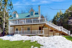 a large house with a wrap around deck in the snow at Kindred Hollow in Ludlow