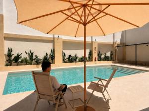 a man sitting in a chair under an umbrella next to a swimming pool at Maritime Coliving Valencia in Valencia