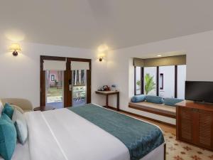 a bedroom with a large bed and a television at Novotel Goa Dona Sylvia Resort in Cavelossim