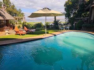 a swimming pool with an umbrella and chairs and tables at Woodpecker cottage in Hartbeespoort