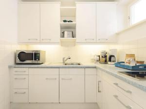 a white kitchen with white cabinets and a microwave at Kliffsand-68 in Kampen