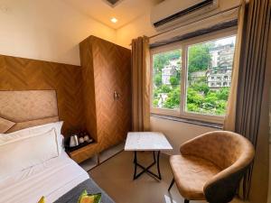 a bedroom with a bed and a chair and a window at Hotel Mahadev Tapovan in Rishīkesh