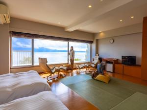 a bedroom with a large window and a woman sitting on the floor at Kyukamura Ibusuki in Ibusuki
