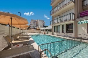a swimming pool with chairs and umbrellas next to a building at Hotel Picobello Pineta in Lido di Jesolo