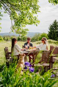 three people sitting at a table with a dog at Baglyashegy Vendégház in Sümeg