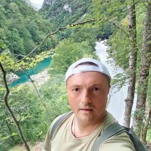 a man in a hat standing in front of a river at Djedova koliba in Žabljak