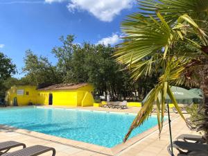 a pool with a yellow house and a palm tree at Domaine Les Chênes Blancs in Saint-Saturnin-lès-Apt