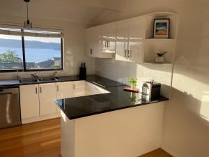 a kitchen with white cabinets and a black counter top at 3BR Retreat with Sunset Views over Brisbane Water in Green Point +3 photos